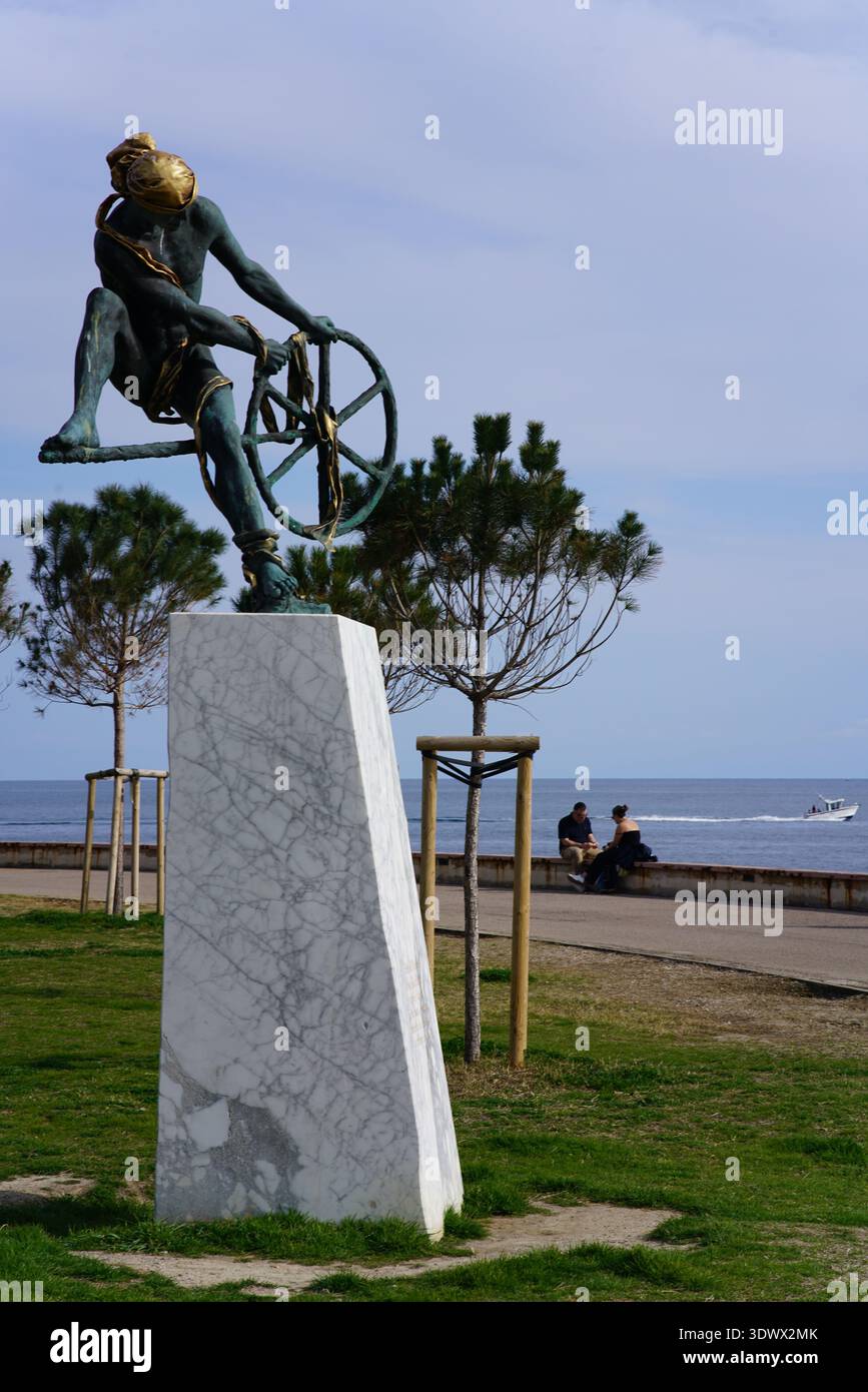 Statua di bronzo di donna con ruota rotante sul lungomare con alberi di pino e vista sull'oceano. Mentone, Francia Foto Stock