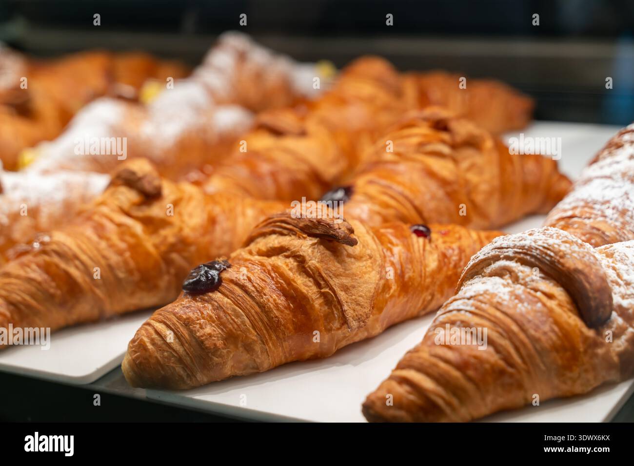 Croissant freschi con crosta dorata e strati delicati poggiano su un vassoio Alcuni dolci sono conditi con zucchero o marmellata, creando un invitante e appetizi Foto Stock