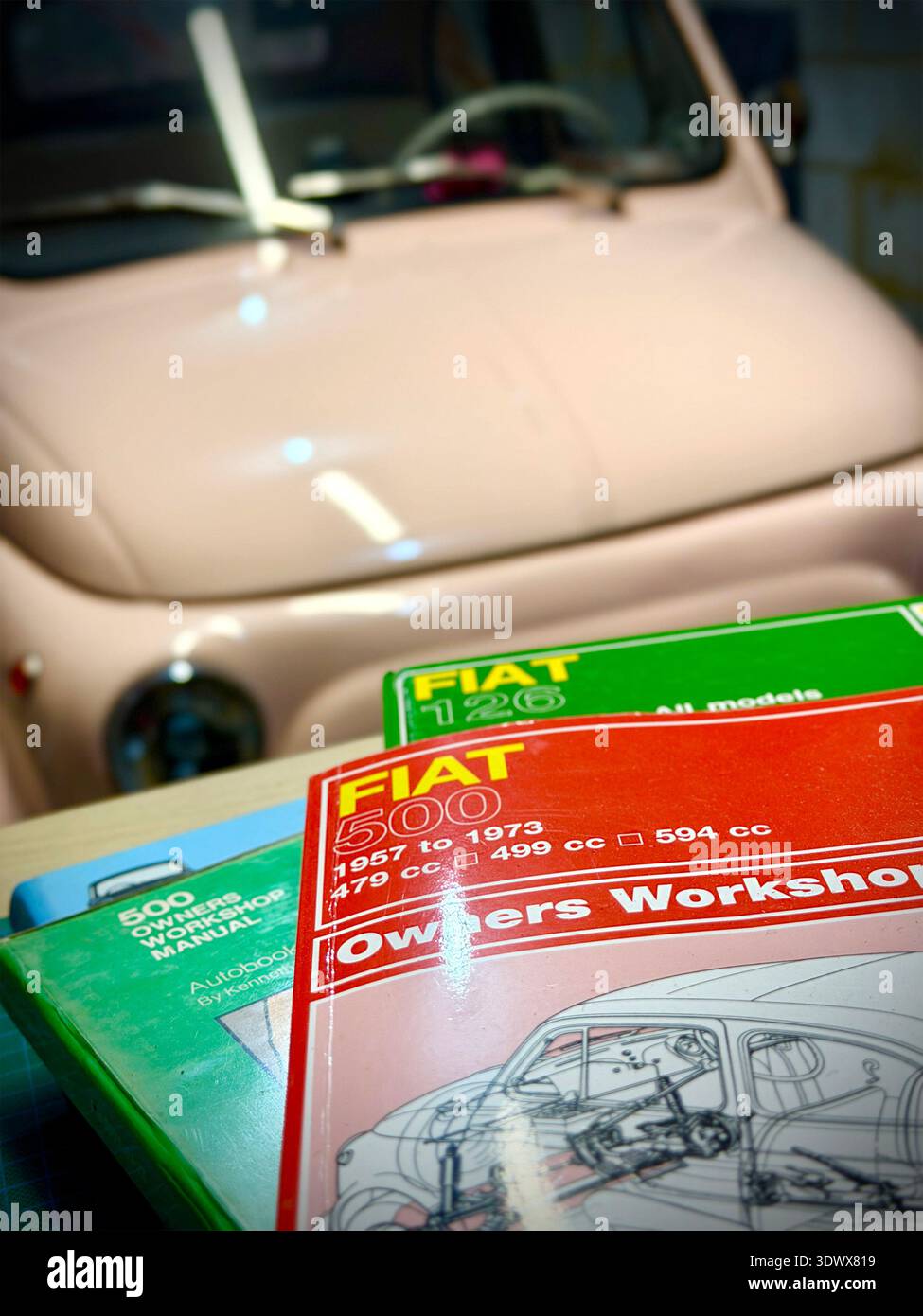 Primo piano dei manuali d'officina di Fiat 500 e Fiat 126 haynes impilati di fronte a una Fiat 500 classica e rosa pallido d'epoca Foto Stock
