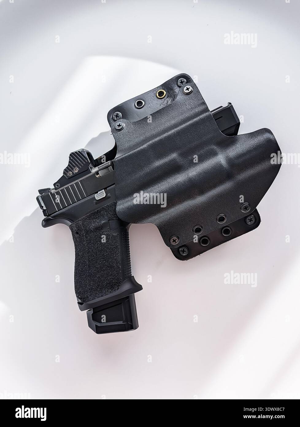 Moderna pistola tattica con mirino rosso e luce per armi in una custodia Kydex nera, con impugnatura a stipite e caricatore esteso. Foto Stock