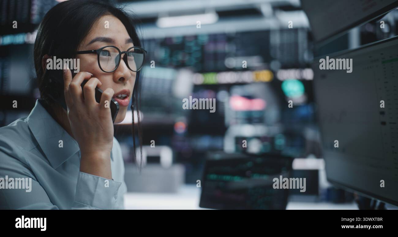 Ansious Asian Female Trader Talking on smartphone during Stock Market Crash in Digital Office. La donna emotiva reagisce con shock e ansia mentre discute di un improvviso calo del prezzo delle azioni sul telefono cellulare. Foto Stock