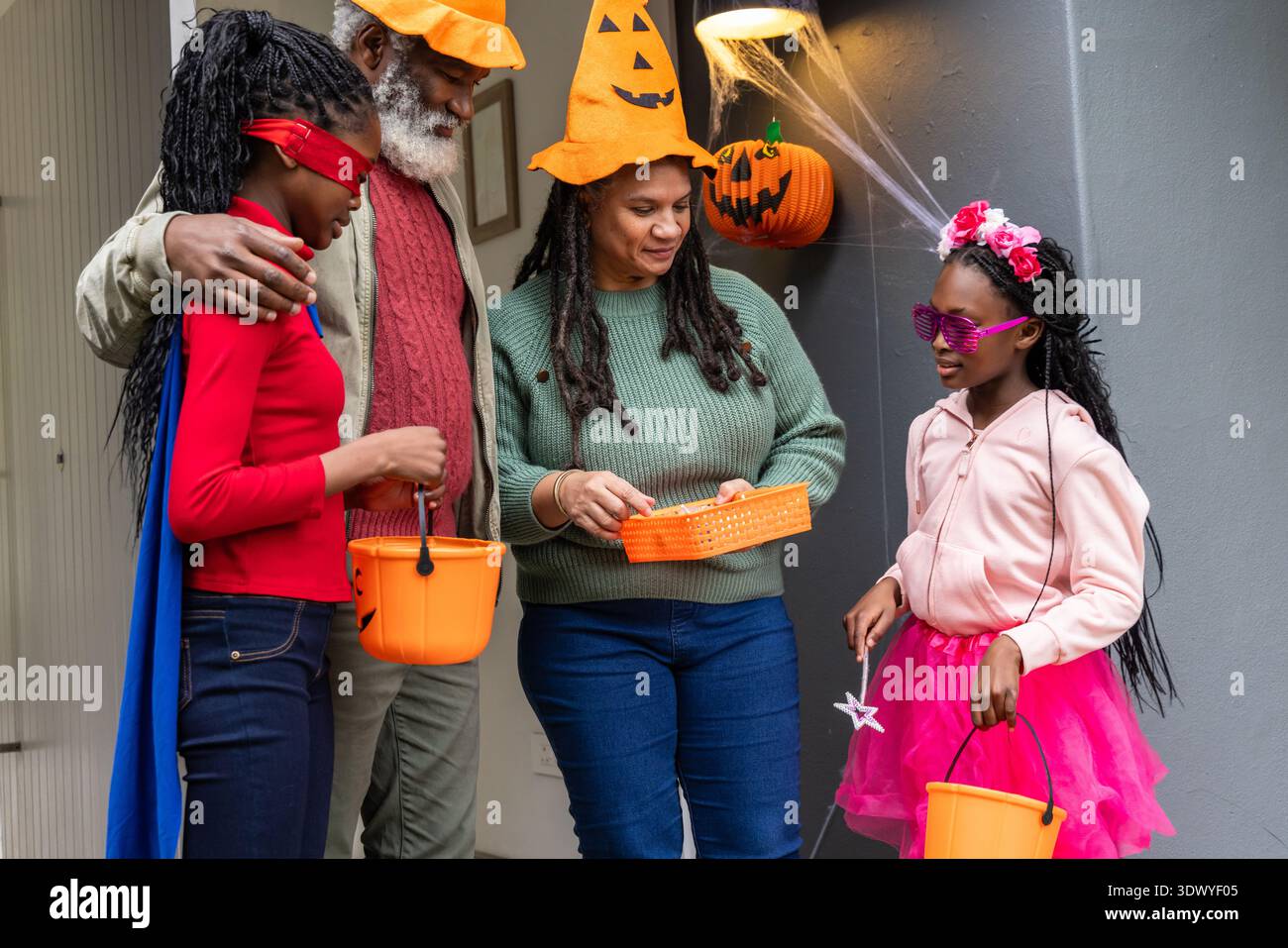 Riunione di famiglia afroamericana su portico con secchi arancioni, vassoio di caramelle, donna che indossa un cappello Foto Stock