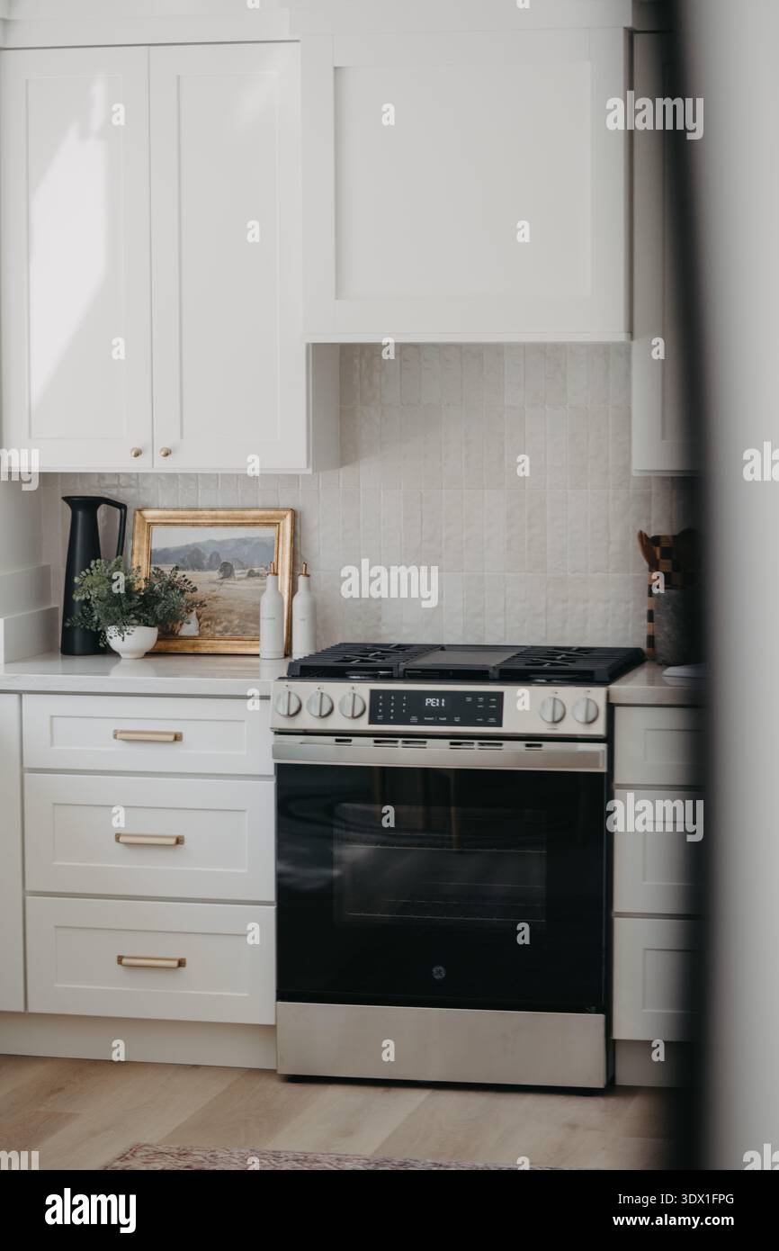 Gli interni luminosi e moderni della cucina presentano mobili bianchi, forno incorporato, spruzzi di marmo e un design minimalista pulito in una casa contemporanea. Foto Stock
