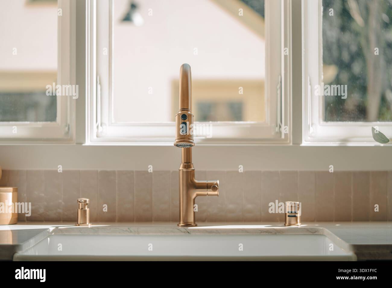 Primo piano di rubinetti da cucina in ottone e lavabo in grembiule in una cucina residenziale moderna e luminosa. Foto Stock