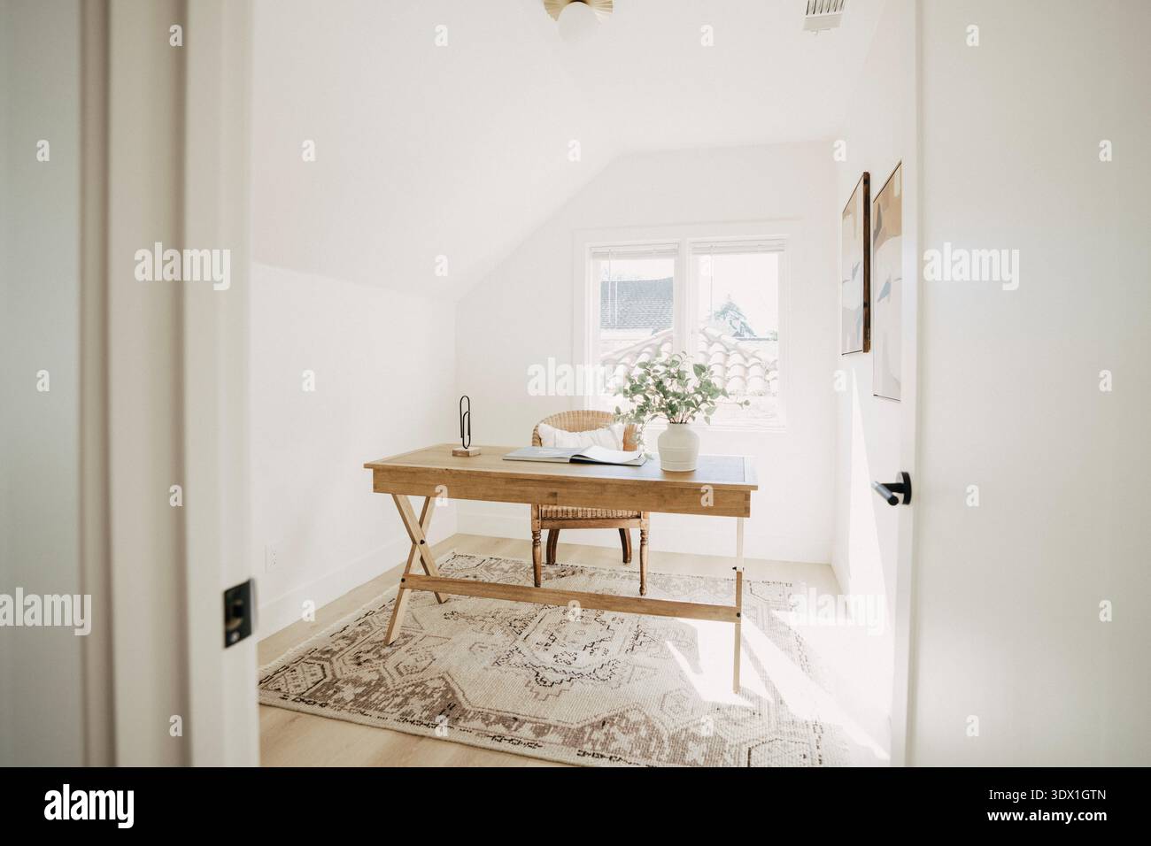 Interni luminosi e minimalisti con scrivania in legno, sedia e luce naturale dalle finestre in una moderna casa residenziale. Foto Stock
