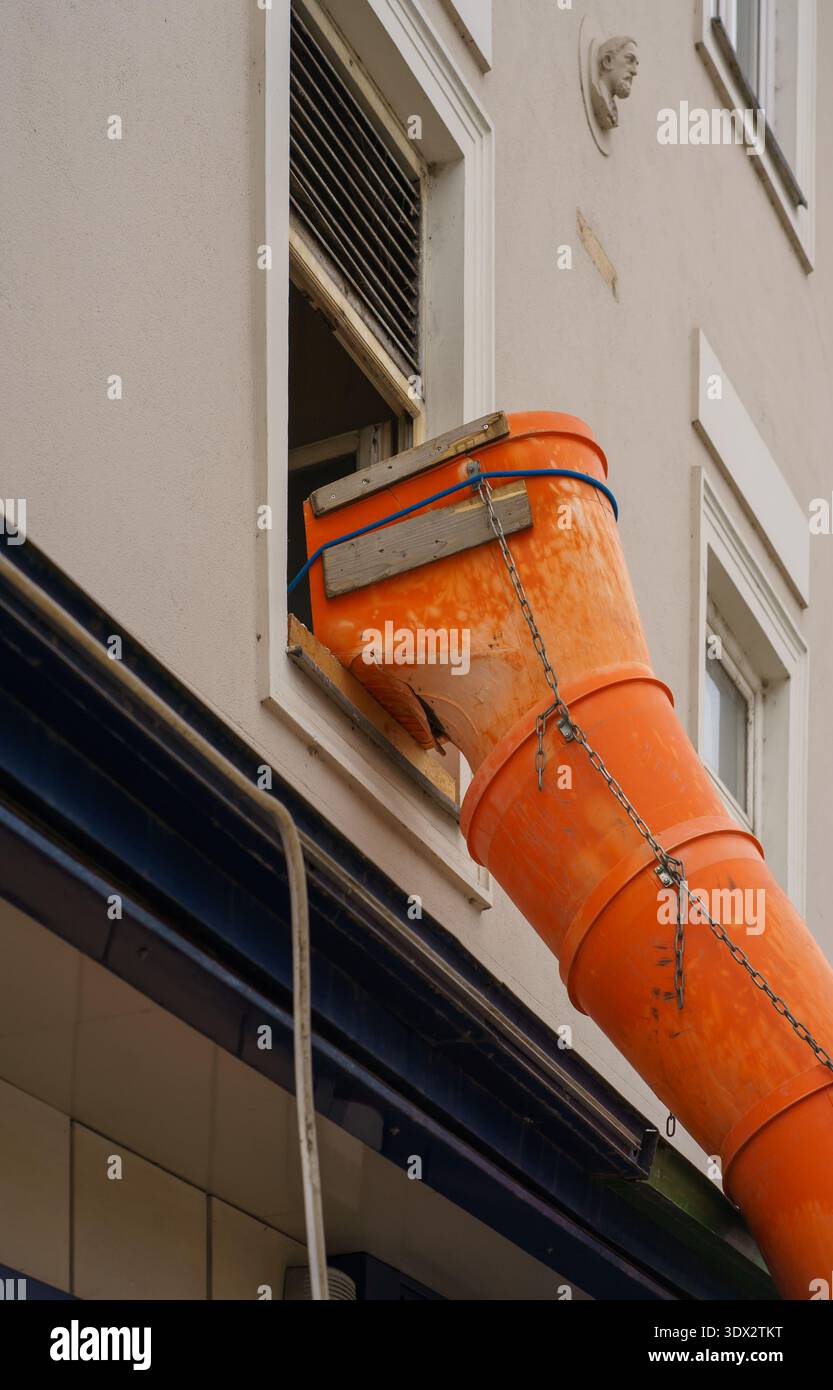 Scivolo per detriti in plastica fissato con catene e legno alla finestra dell'edificio residenziale. Ristrutturazione esterna, lavori di riparazione e dettagli di costruzione urbana Foto Stock