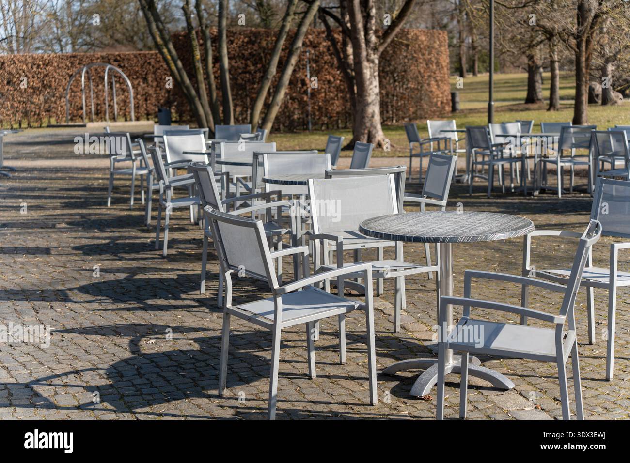 In un'area del parco pavimentata sono disposte più sedie e tavoli. La luce solare intensa mette in risalto il layout strutturato degli esterni. Foto Stock