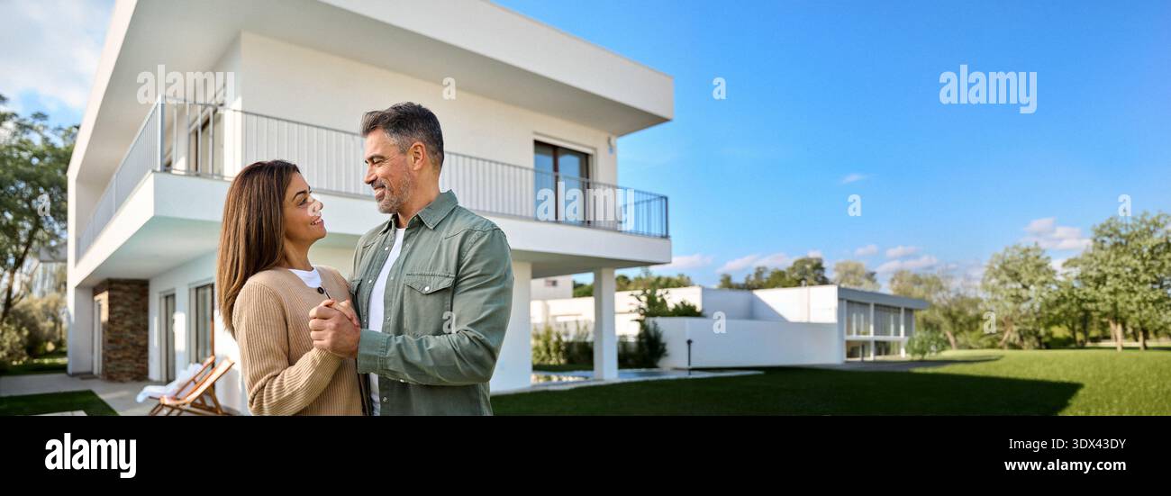 Felice sorridente coppia di mezza età nuovi acquirenti di proprietà in piedi fuori casa. Foto Stock