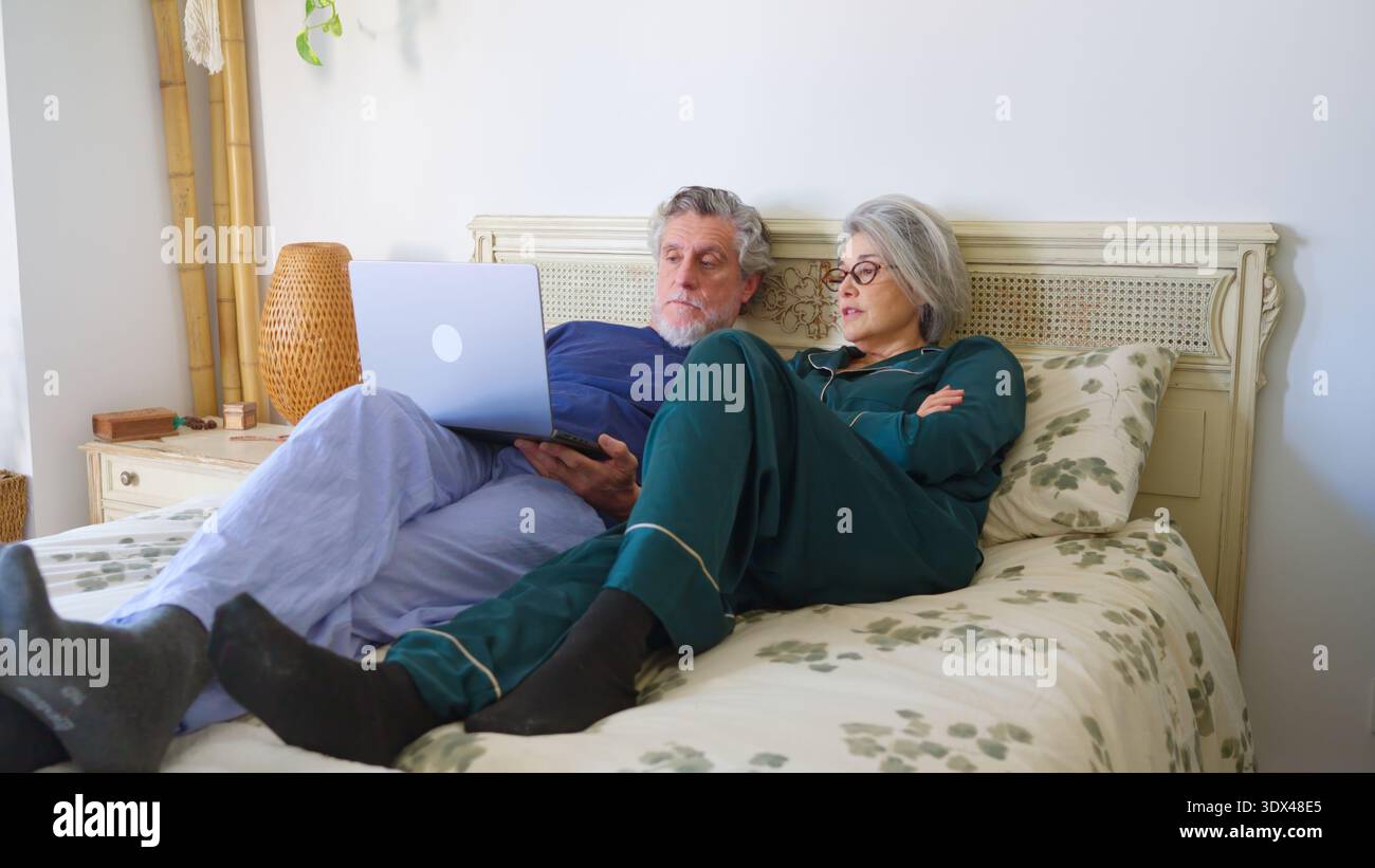 Una coppia anziana a letto che guarda il portatile insieme Foto Stock