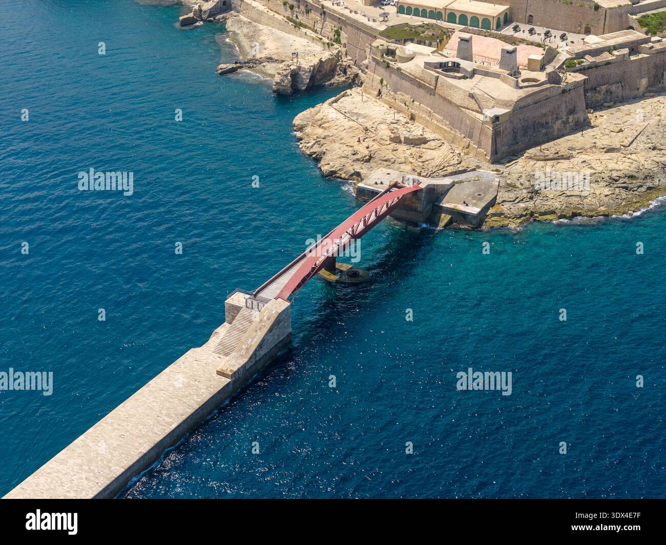Il ponte di Sant'Elmo si estende sull'ingresso del porto di Fort Sant'Elmo a la Valletta, con archi rossi in acciaio sopra una frangiflutti e un profondo blu del Mar Mediterraneo. Foto Stock