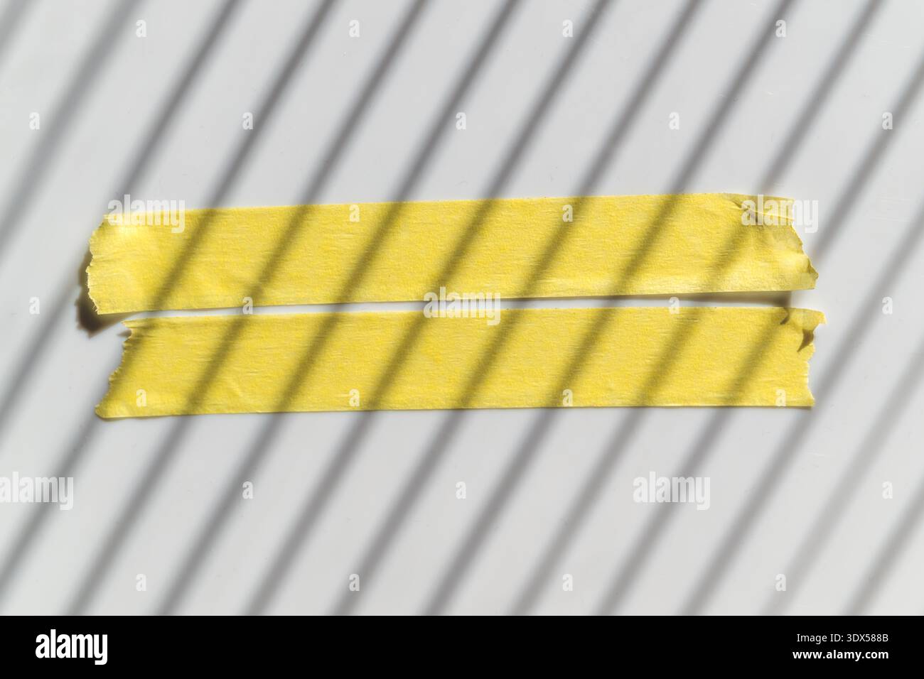 Nastro di mascheratura giallo crespato su uno sfondo chiaro con ombre a strisce, texture astratta e illuminazione grafica. Vista dall'alto. Foto Stock