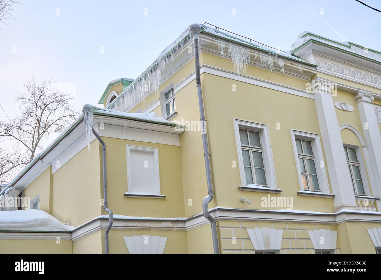 Ghiaccioli appesi al tetto dello storico edificio giallo sotto il cielo invernale Foto Stock