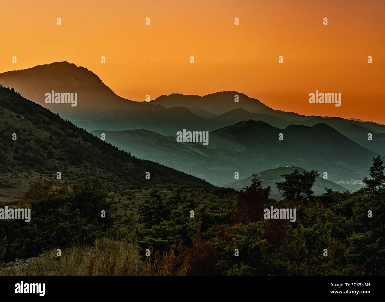 Un paesaggio di montagna a strati al tramonto crea una scena tranquilla con colline ondulate e un cielo dalle tonalità calde. Abruzzo, Italia, Europa Foto Stock