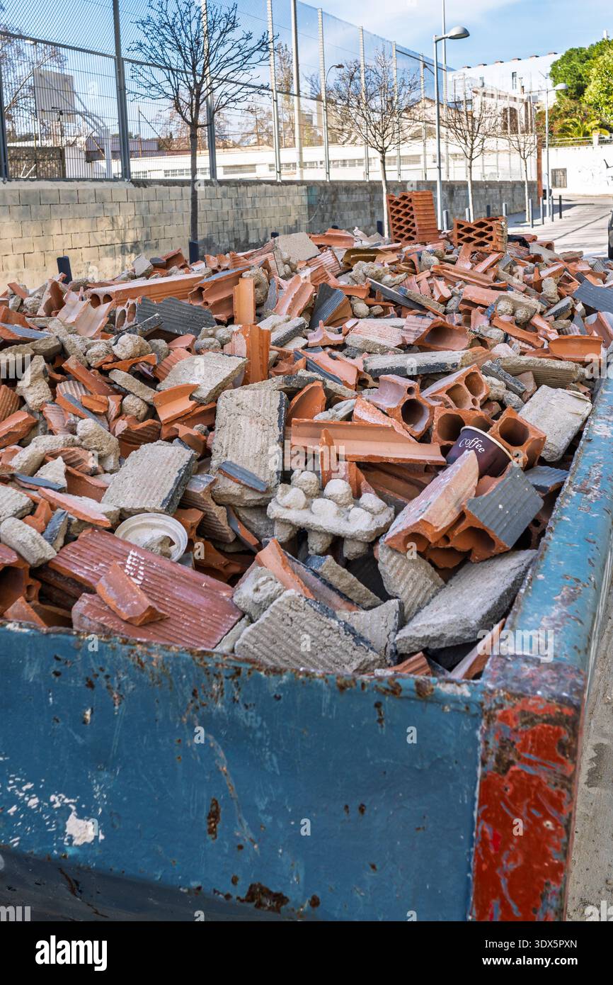 Un contenitore blu per rifiuti industriali riempito di detriti da costruzione, mattoni rotti e calcestruzzo provenienti da un cantiere di demolizione. Foto Stock