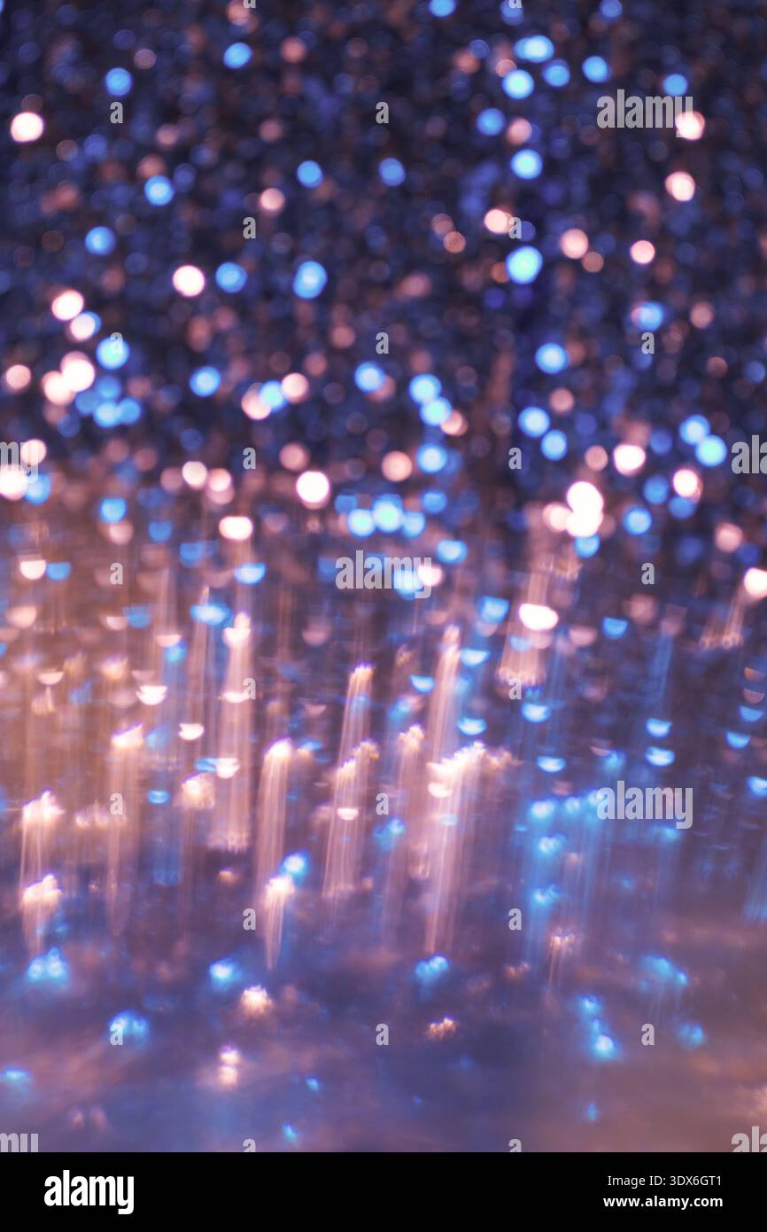Un'immagine astratta con uno sfondo bokeh luminoso in sfumature di blu e arancione, che crea un effetto scintillante con una texture luccicante. Perfetto per d Foto Stock