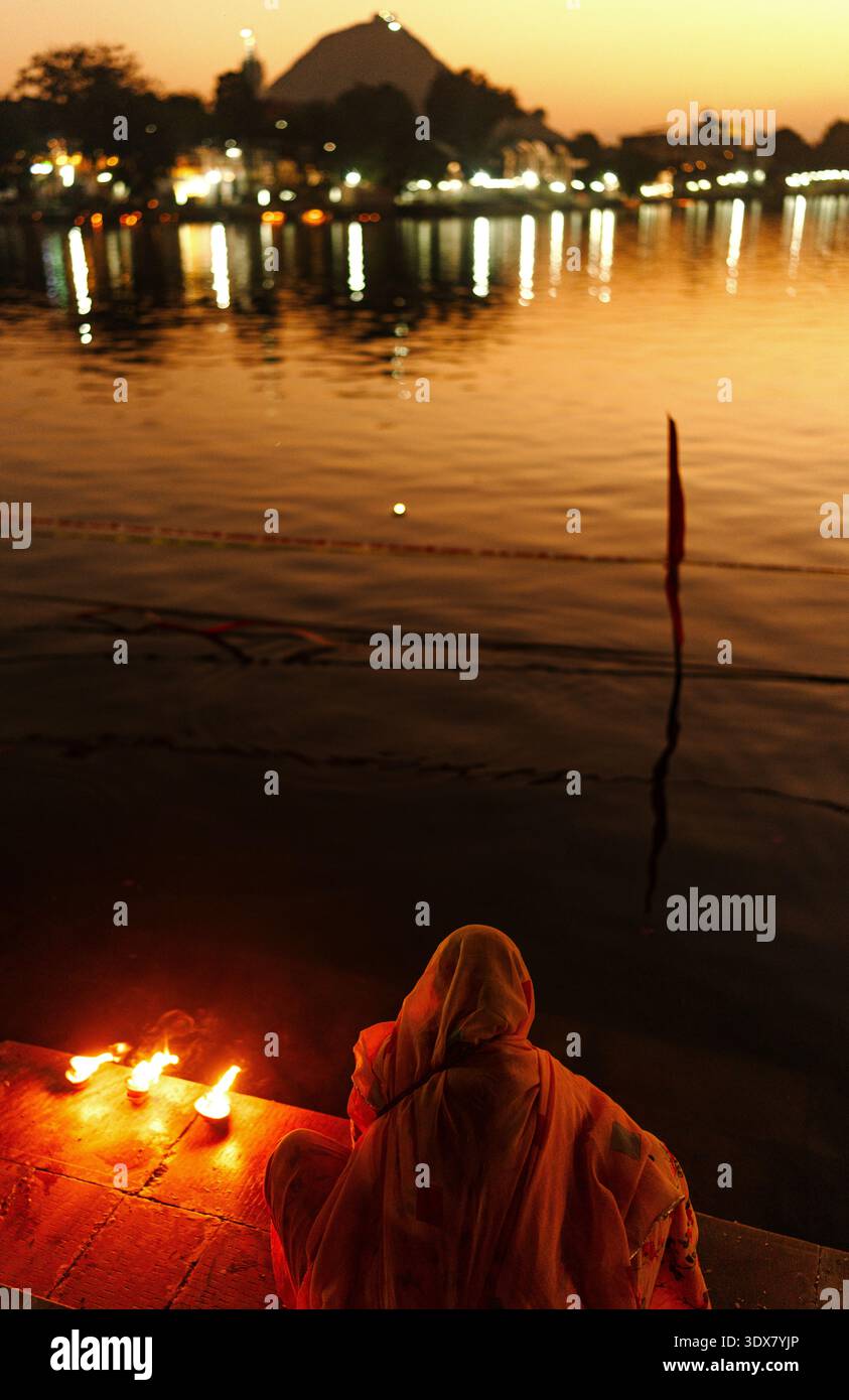 Devoto indù che offre preghiere serali con lampade ad olio accanto al lago Pushkar al crepuscolo, Rajasthan, India Foto Stock