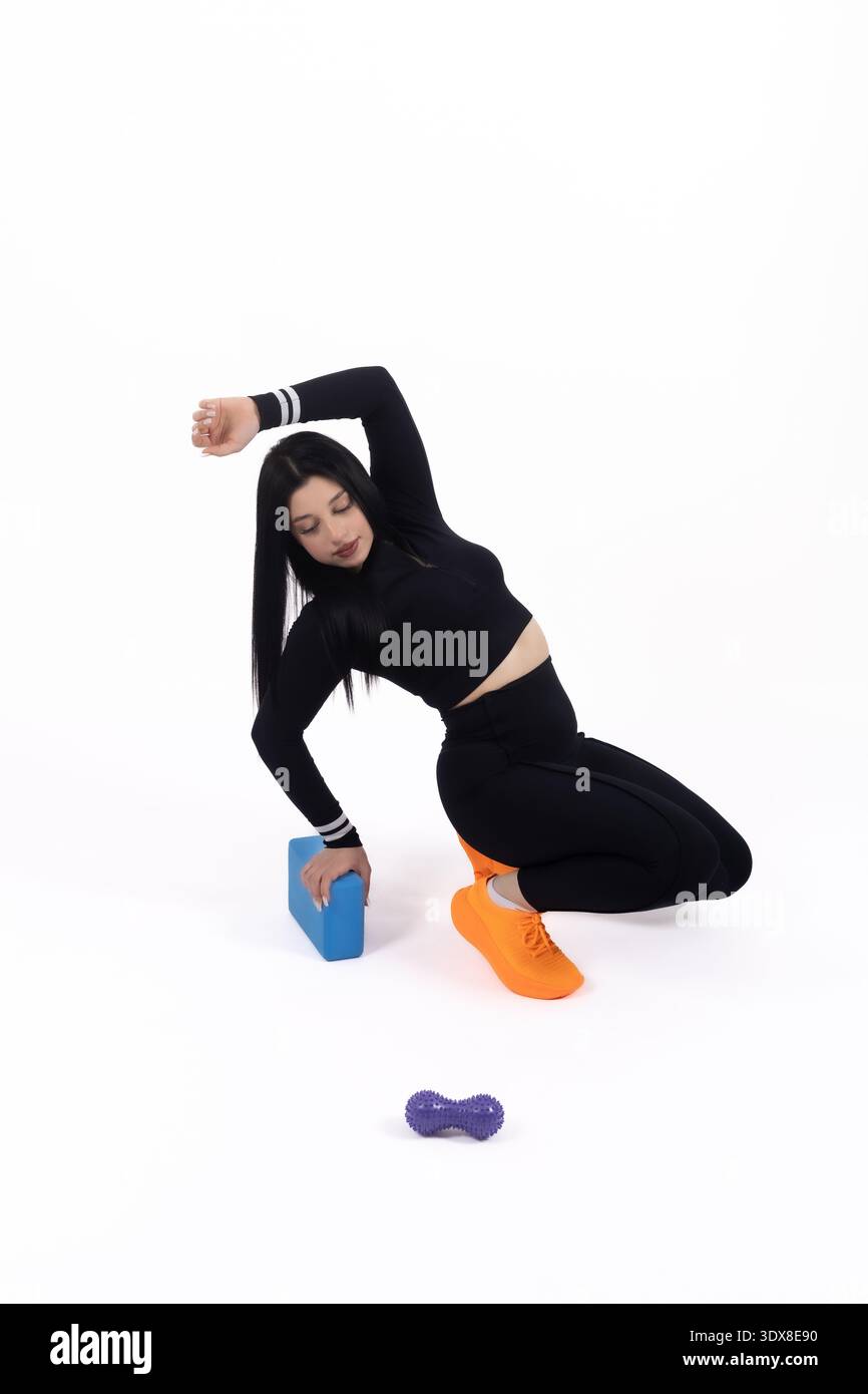 Vesti la donna con un abbigliamento sportivo nero inginocchiato su un pavimento bianco in studio Foto Stock