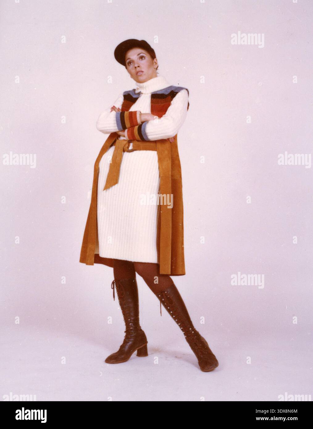Modello che indossa un abito in maglione dolcevita a coste con un gilet longuette in pelle scamosciata color abbronzatura con pannelli a righe tonalità terra, un berretto piatto coordinato e stivali con lacci marroni, Italia anni '1970 Foto Stock