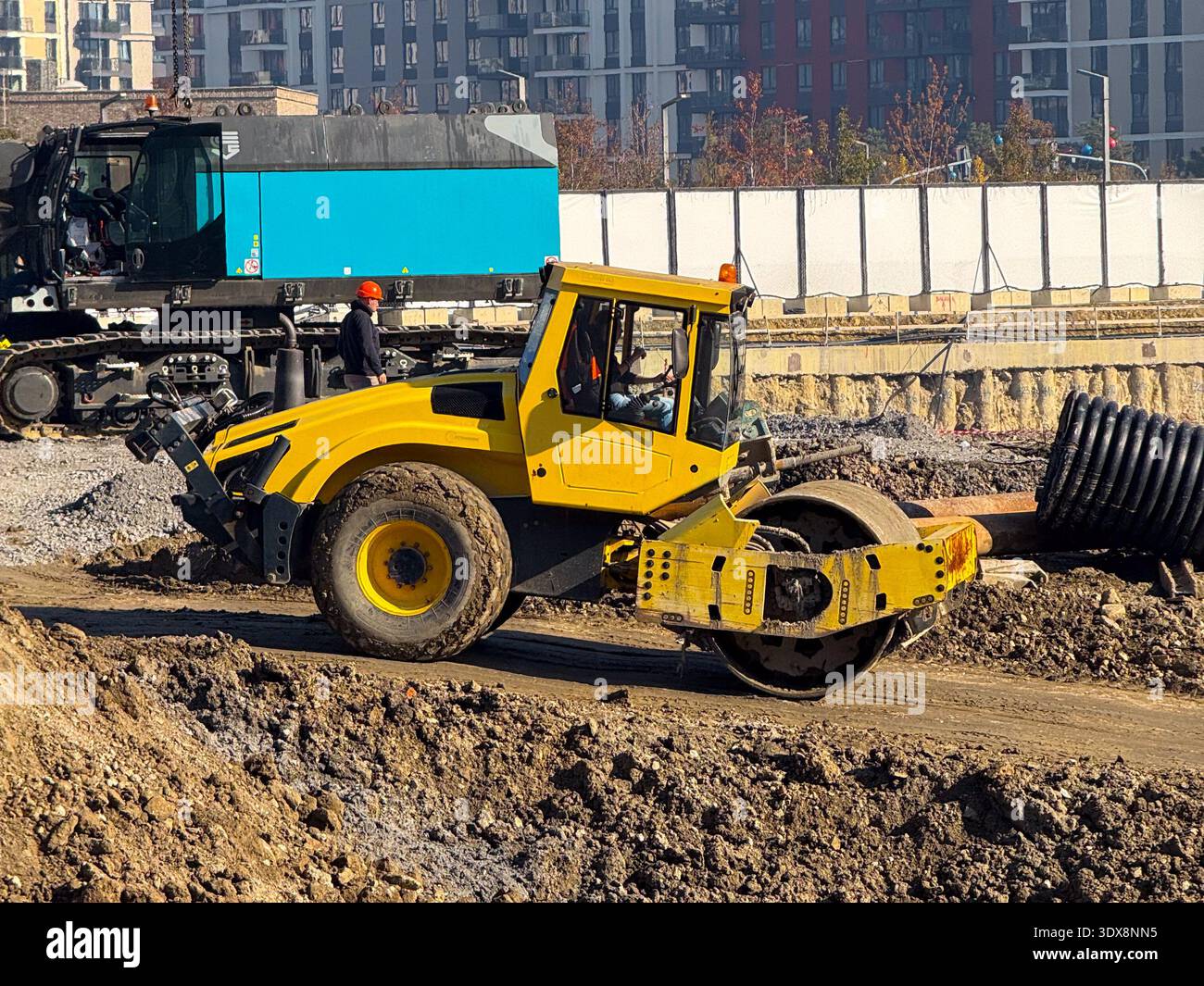 Rullo giallo per terreno in cantiere con edifici alti sullo sfondo. Sviluppo urbano, macchinari stradali, miglioramento delle infrastrutture e. Foto Stock