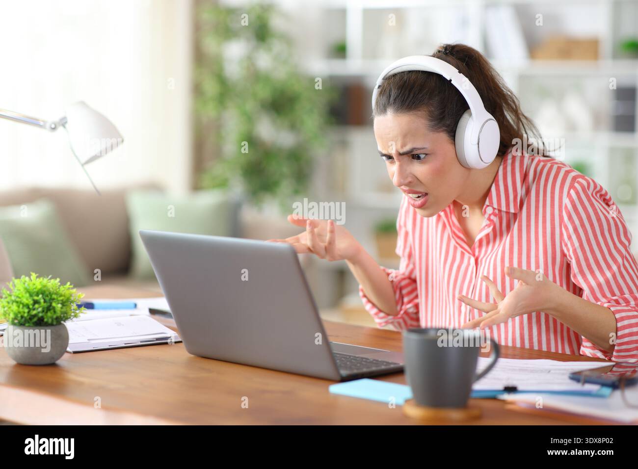 Tele worker stressato che effettua videochiamate utilizzando l'auricolare e il computer portatile che lavorano a casa Foto Stock