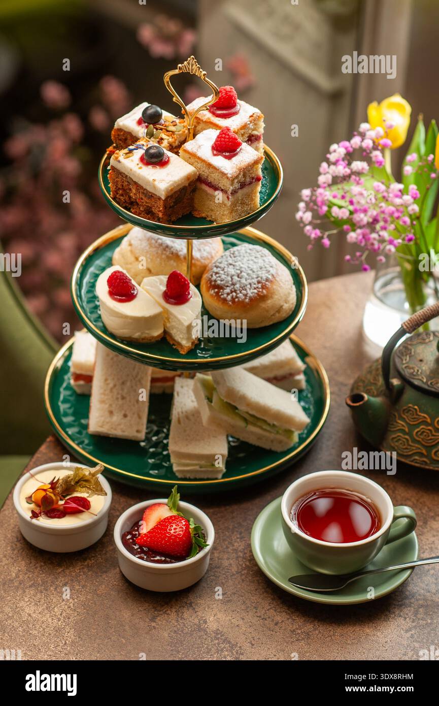 Un classico set da tè pomeridiano con tre strati verdi ripieni di finger sandwich, focaccine e torte assortite, serviti con una tazza di tè nero e. Foto Stock