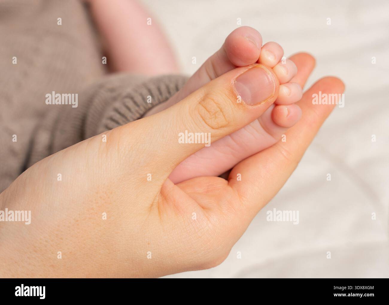 Primo piano di un genitore che tiene delicatamente in mano un neonato, le dita dei piedi sono minuscole. L'illuminazione soffusa e le tonalità calde creano un'atmosfera intima e toccante adatta a temi Foto Stock