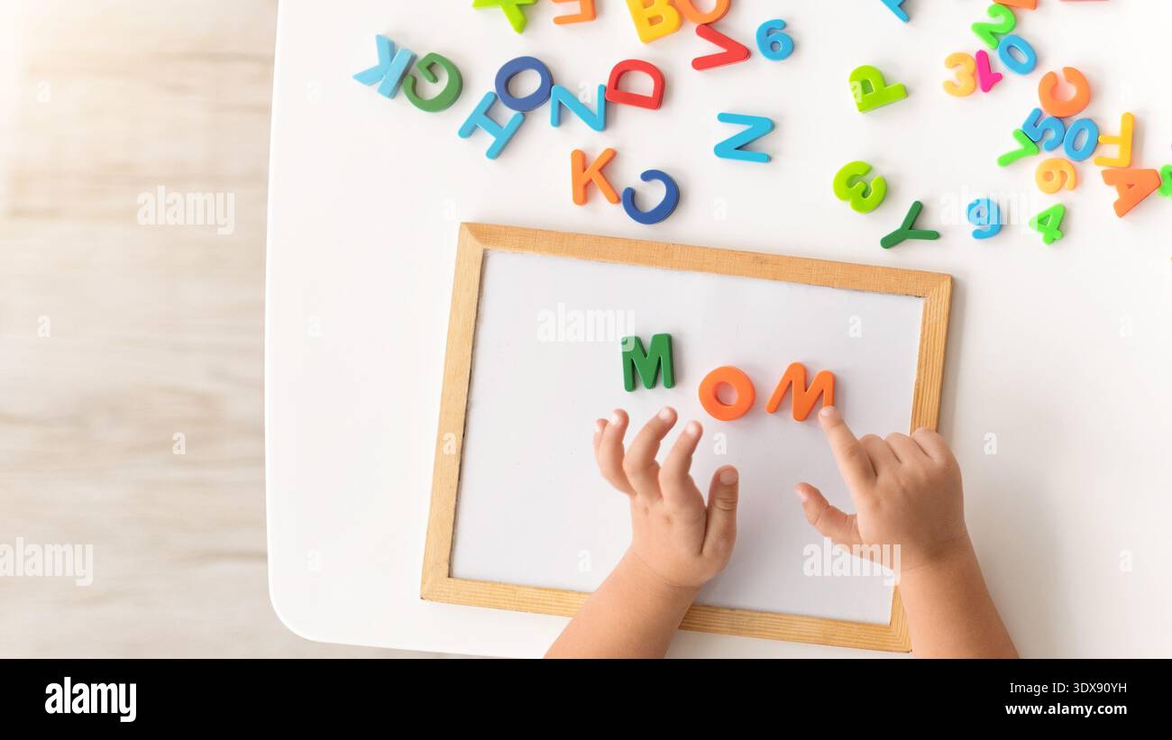 Il bambino esplora le lettere su un tavolo mentre scrive la parola mamma con le lettere in schiuma colorate Foto Stock