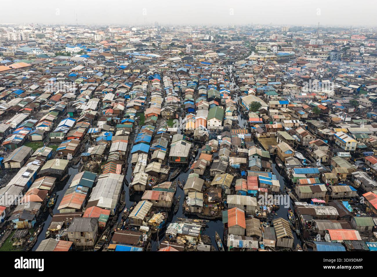 Vista aerea di un vasto insediamento dove gli edifici incontrano l'acqua, creando un arazzo di texture e toni sotto un cielo nebbioso, Lagos, Lagos, Nigeri Foto Stock