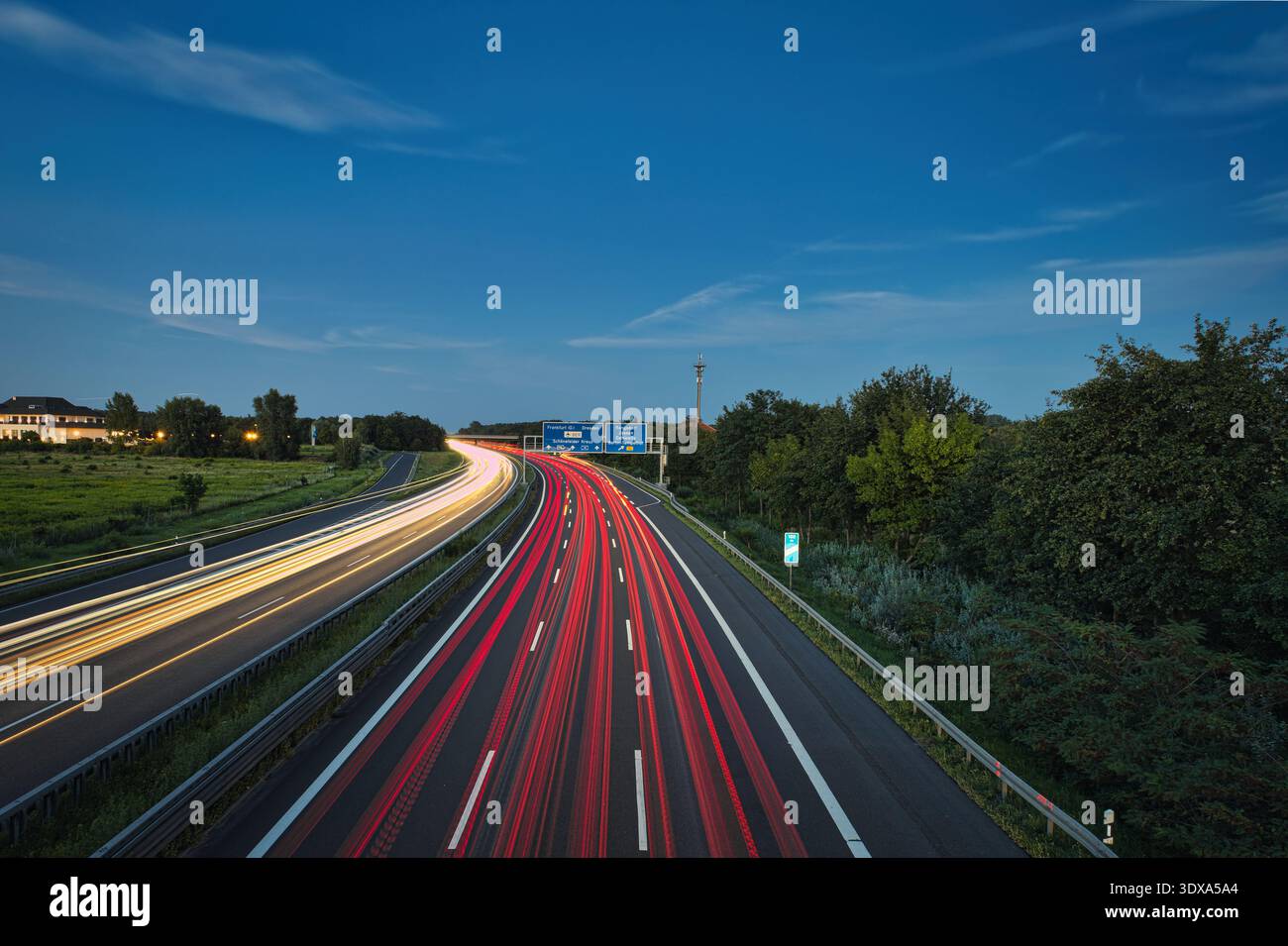 Lunga esposizione del traffico autostradale al tramonto, con percorsi leggeri dai fari e dalle luci posteriori dell'auto contro il cielo del tramonto e le sagome degli alberi Foto Stock