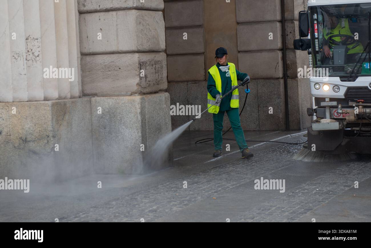 Milano Italia 27 febbraio 2026: Un operaio dei servizi comunali pulisce il fondo stradale con un getto d'acqua ad alta pressione, indossando un panno di sicurezza ad alta visibilità Foto Stock