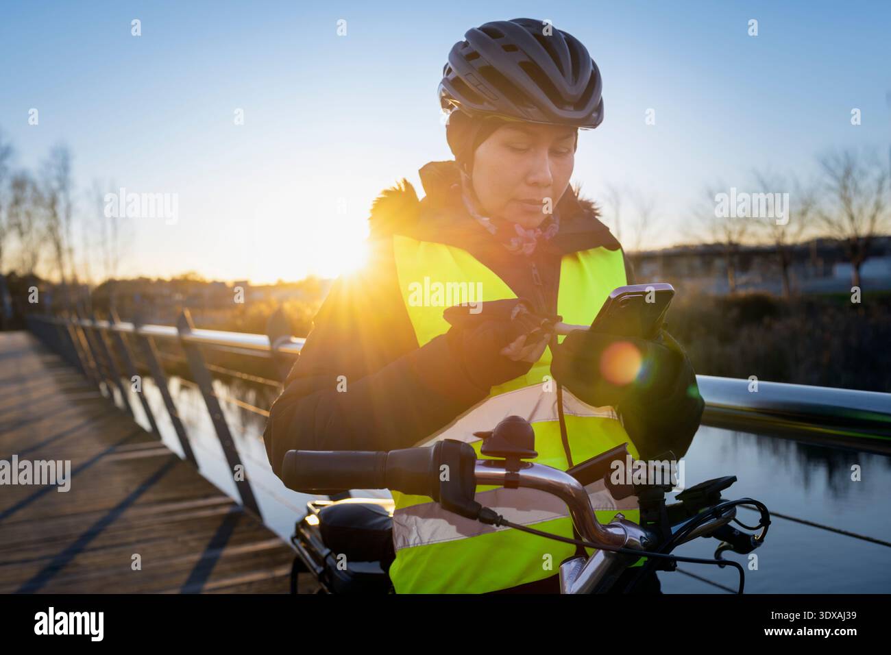 Ciclista donna che utilizza lo smartphone mentre si trova vicino a una ringhiera sul ponte Foto Stock