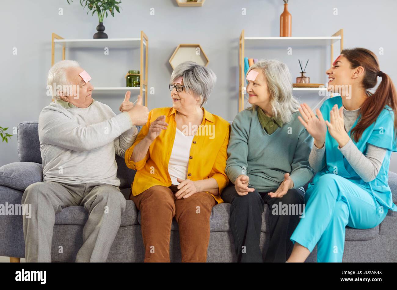 Felice sorridente anziani che giocano divertente gioco con la giovane infermiera amichevole in casa di riposo. Foto Stock