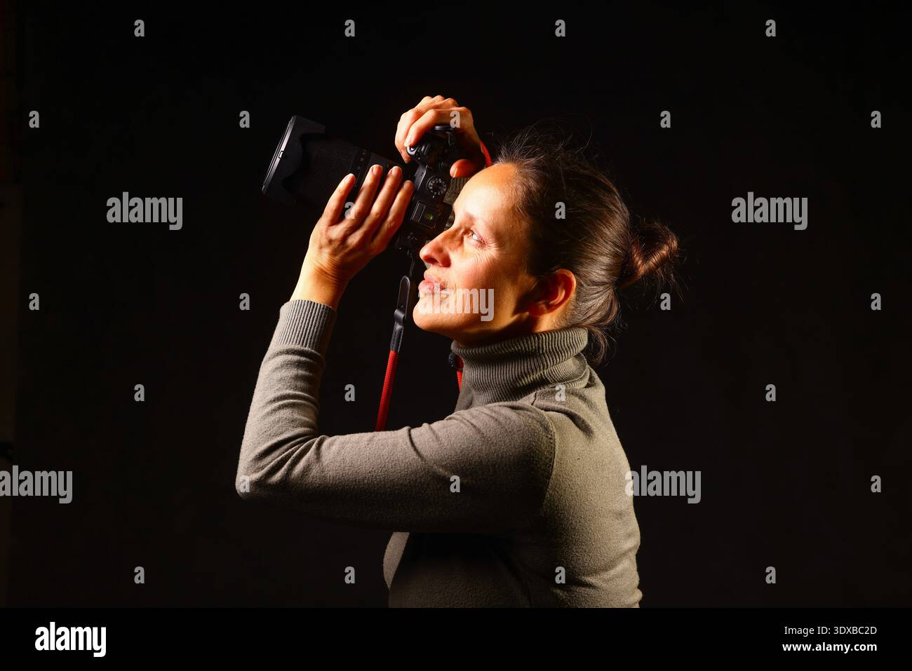 Donna che tiene una fotocamera in un ambiente scuro e minimalista, focalizzata sulla fotografia, attrezzature professionali, lavoro creativo, stile visivo, media e aria condizionata moderni Foto Stock