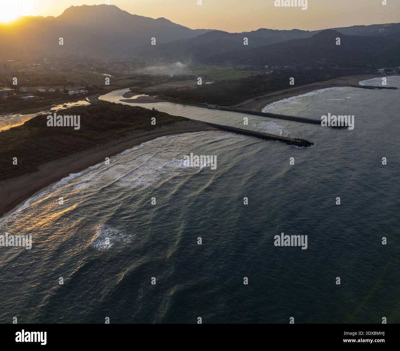 Vista aerea della luce dorata del sole che baciano le acque scure mentre incontrano la riva vicino alle montagne, Keelung, Keelung City, Taiwan. Foto Stock