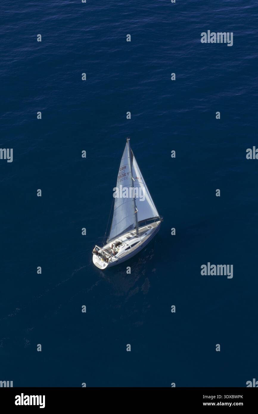 Vista aerea di una barca a vela solitaria che naviga con grazia nel profondo blu del mare, le sue vele bianche contrastano con la vasta distesa d'acqua, Alicante, V. Foto Stock