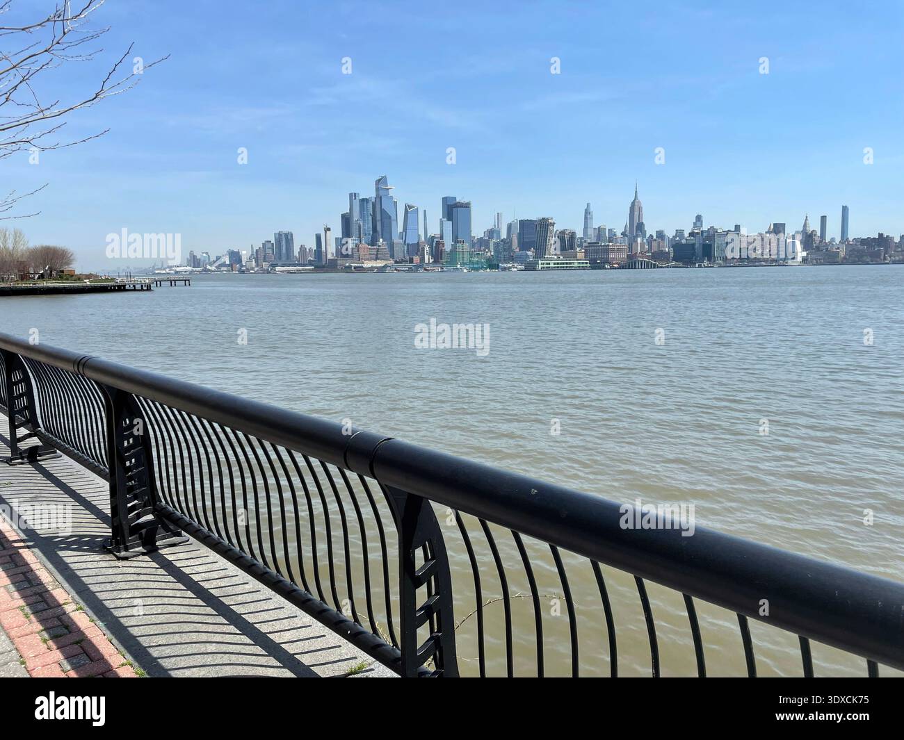 Vista dello skyline di Manhattan attraverso il fiume Hudson dal lungomare di Hoboken nel New Jersey, con una passeggiata lungo il fiume e una ringhiera nell'allegro - Immagine stock catturata con smartphone