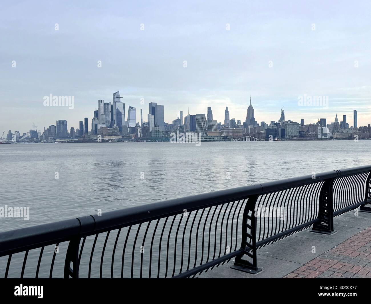 Vista dello skyline di Manhattan attraverso il fiume Hudson dal lungomare di Hoboken nel New Jersey, con una passeggiata lungo il fiume e una ringhiera nell'allegro - Immagine stock catturata con smartphone