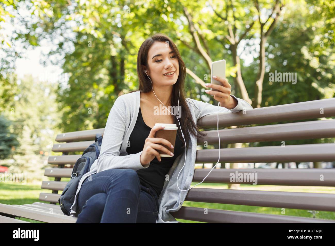 I giovani si godono un caffè e della musica seduti su una panchina del parco Foto Stock