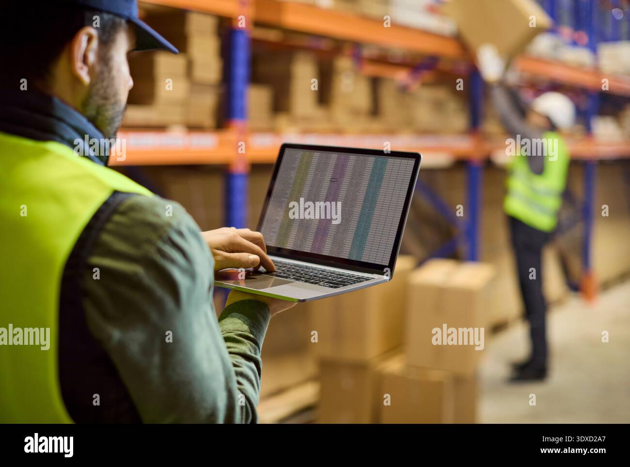 Inventario del magazzino con il lavoratore che utilizza un laptop per tenere traccia delle scorte sugli scaffali Foto Stock