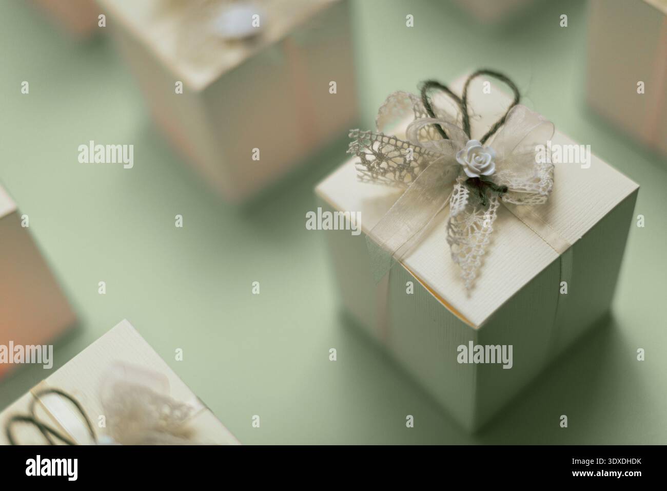 Scatole regalo color crema disposte elegantemente, con fiocchi in pizzo e piccole decorazioni di rose bianche. Ogni scatola è legata con spago, aggiungendo una t rustica Foto Stock