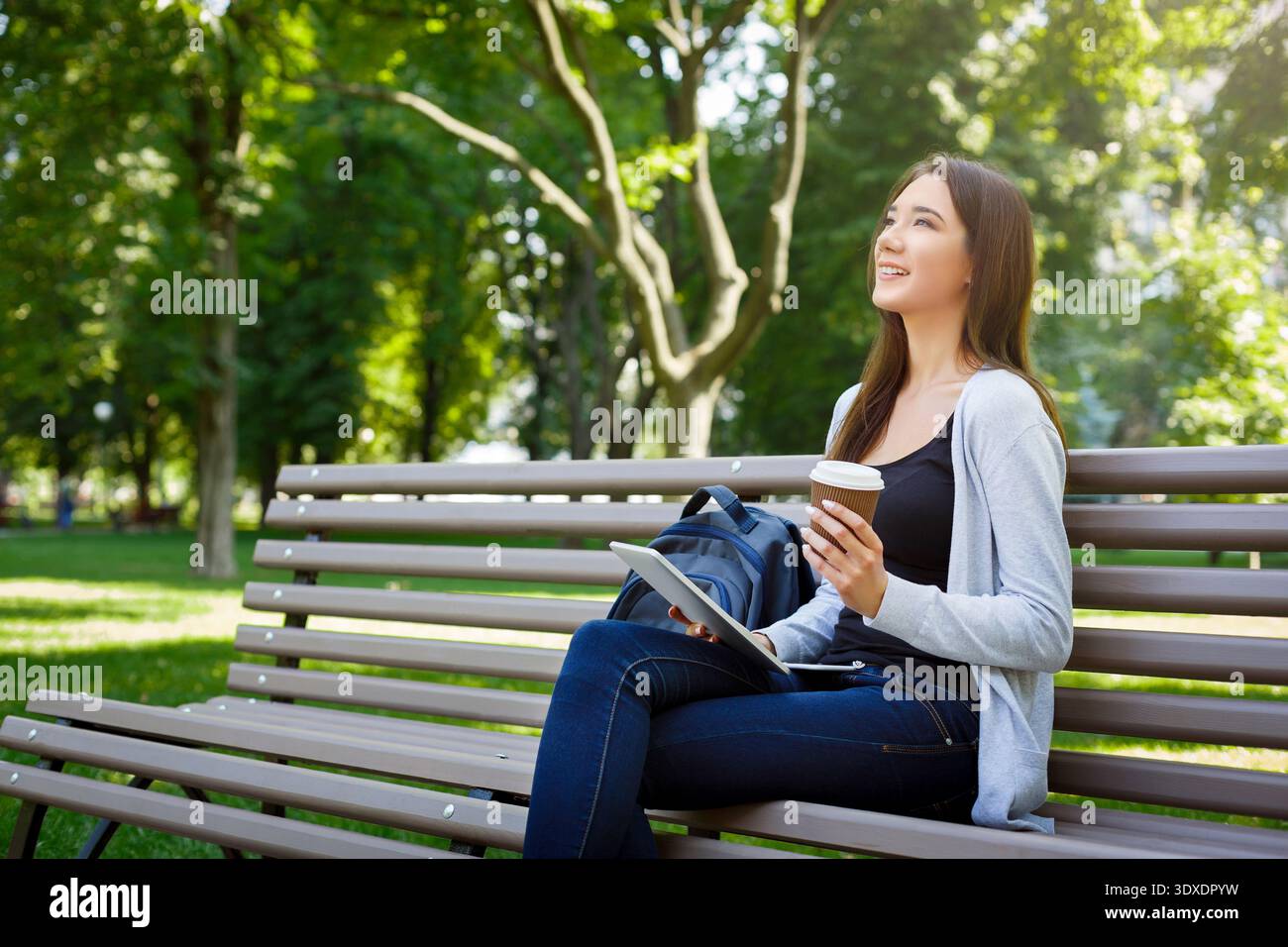 I giovani amano trascorrere il tempo a Park con caffè e tablet seduti sulla panchina durante la stagione soleggiata Foto Stock