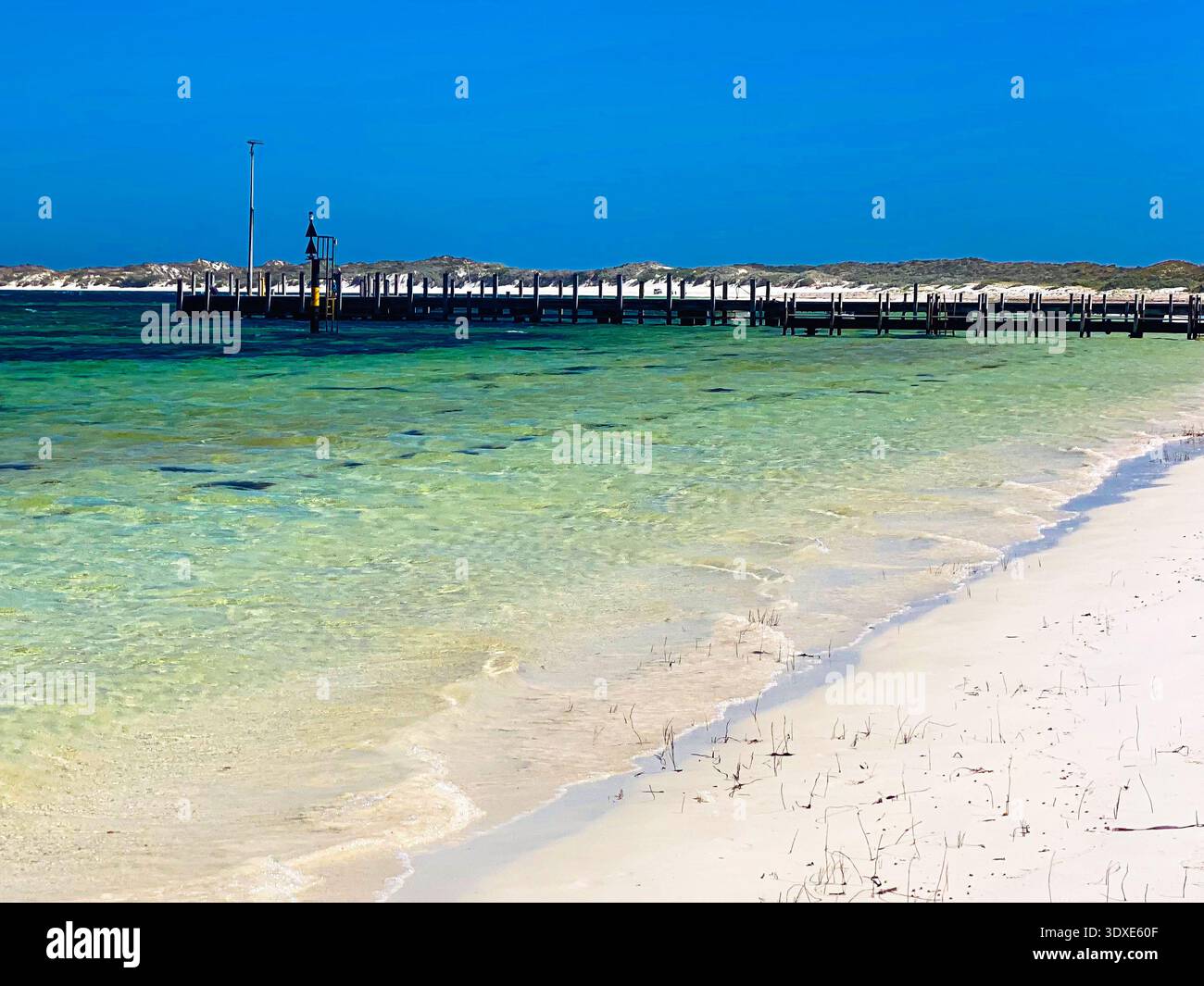 Un lungo molo di legno si estende nell'oceano, circondato da una spiaggia di sabbia e da acque cristalline, evocando serenità e relax. Foto Stock