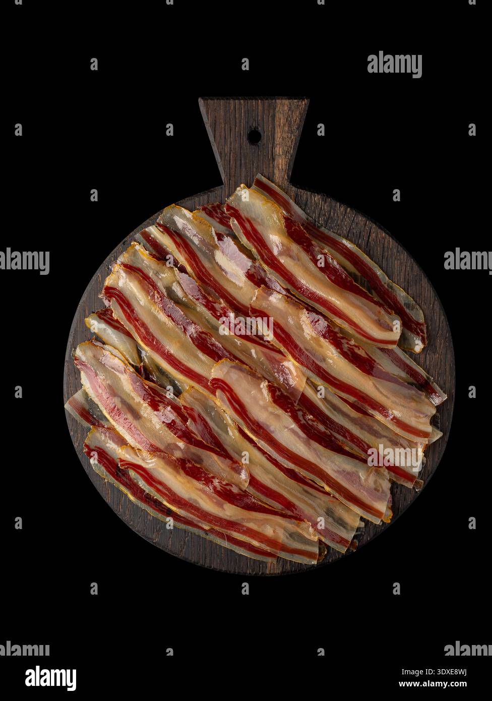 Fette di pancetta a strisce crude su un bordo di legno scuro. Isolata sul nero, vista dall'alto. Copia spazio. Foto Stock