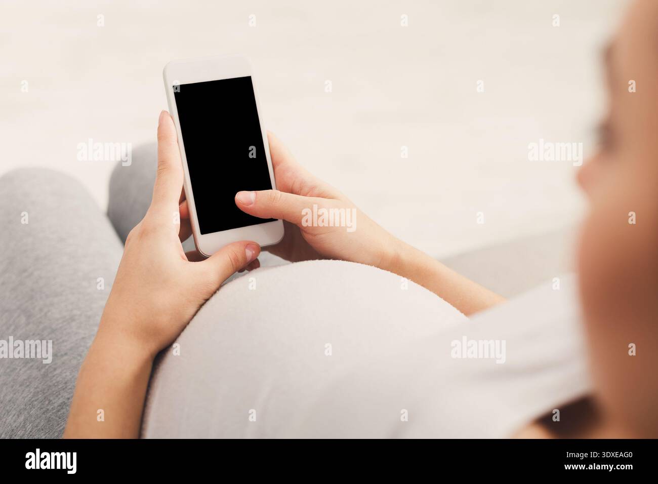 Donna incinta che utilizza lo smartphone mentre si rilassa a casa in un ambiente accogliente Foto Stock