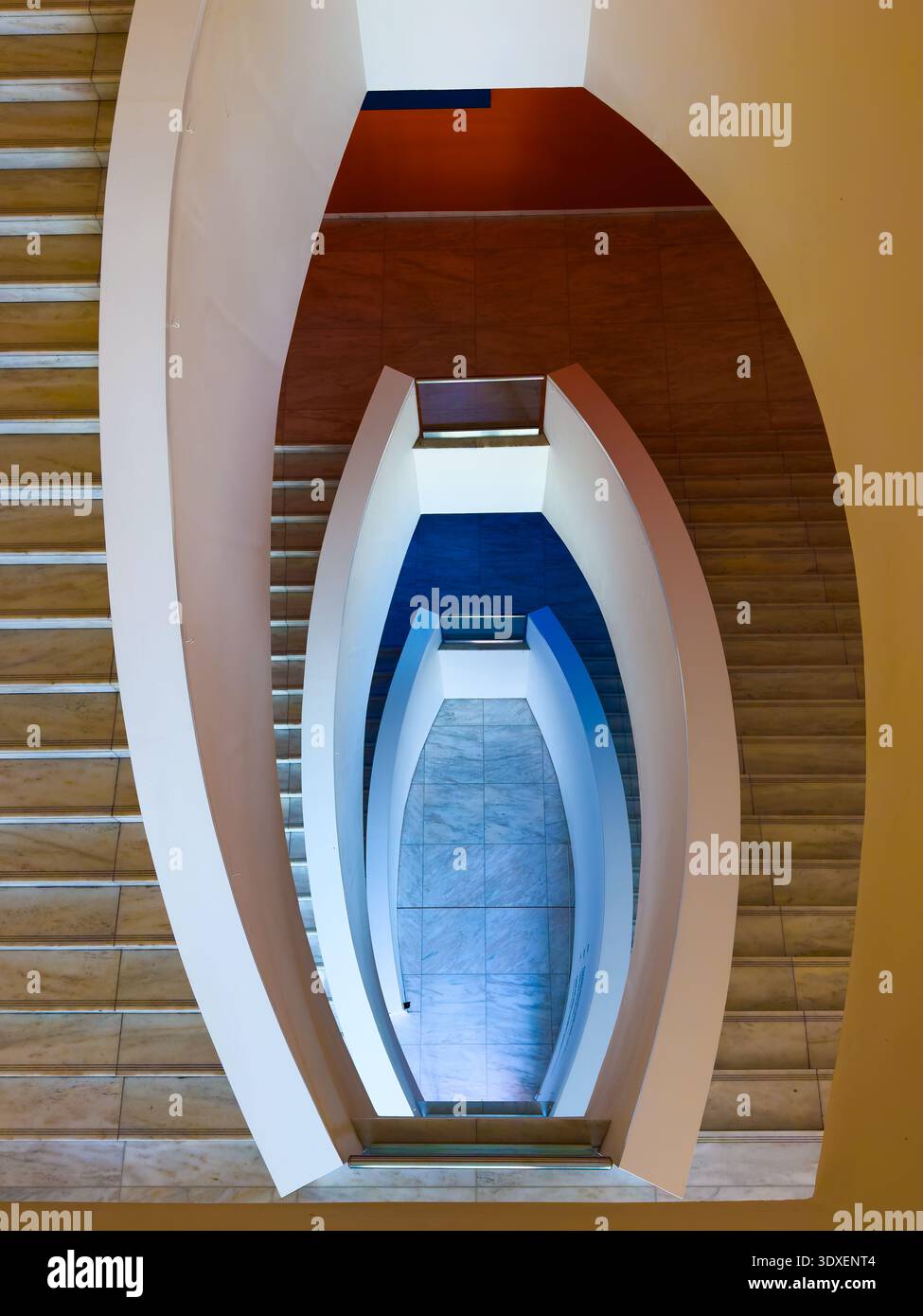 Vista dall'alto della moderna scala curva e dell'architettura geometrica a spirale, linee pulite, simmetria, gradini in marmo, accenti blu. Foto Stock