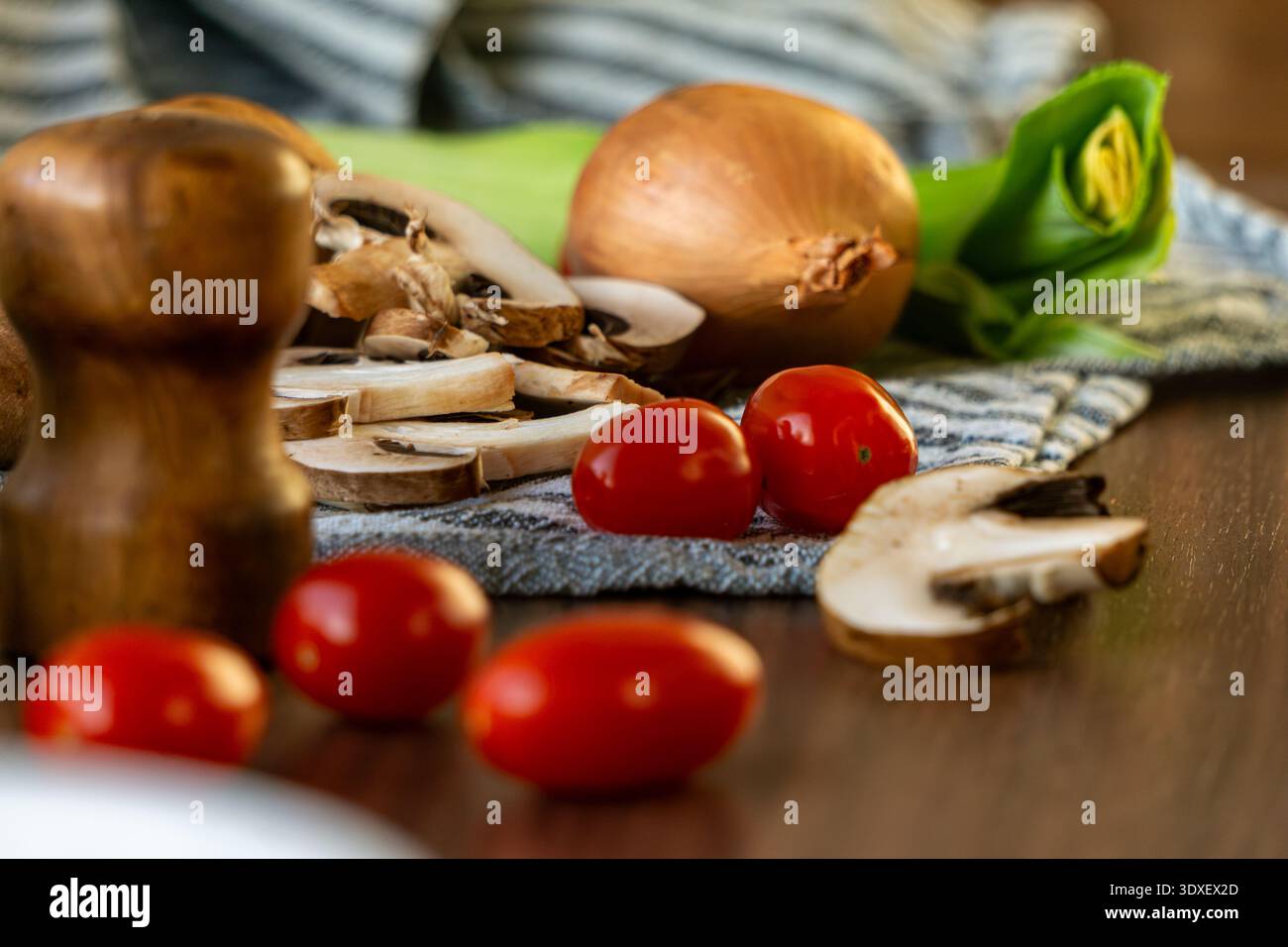 Primo piano di funghi a fette, pomodori ciliegini, cipolla e porri disposti su un tavolo di legno. Foto Stock