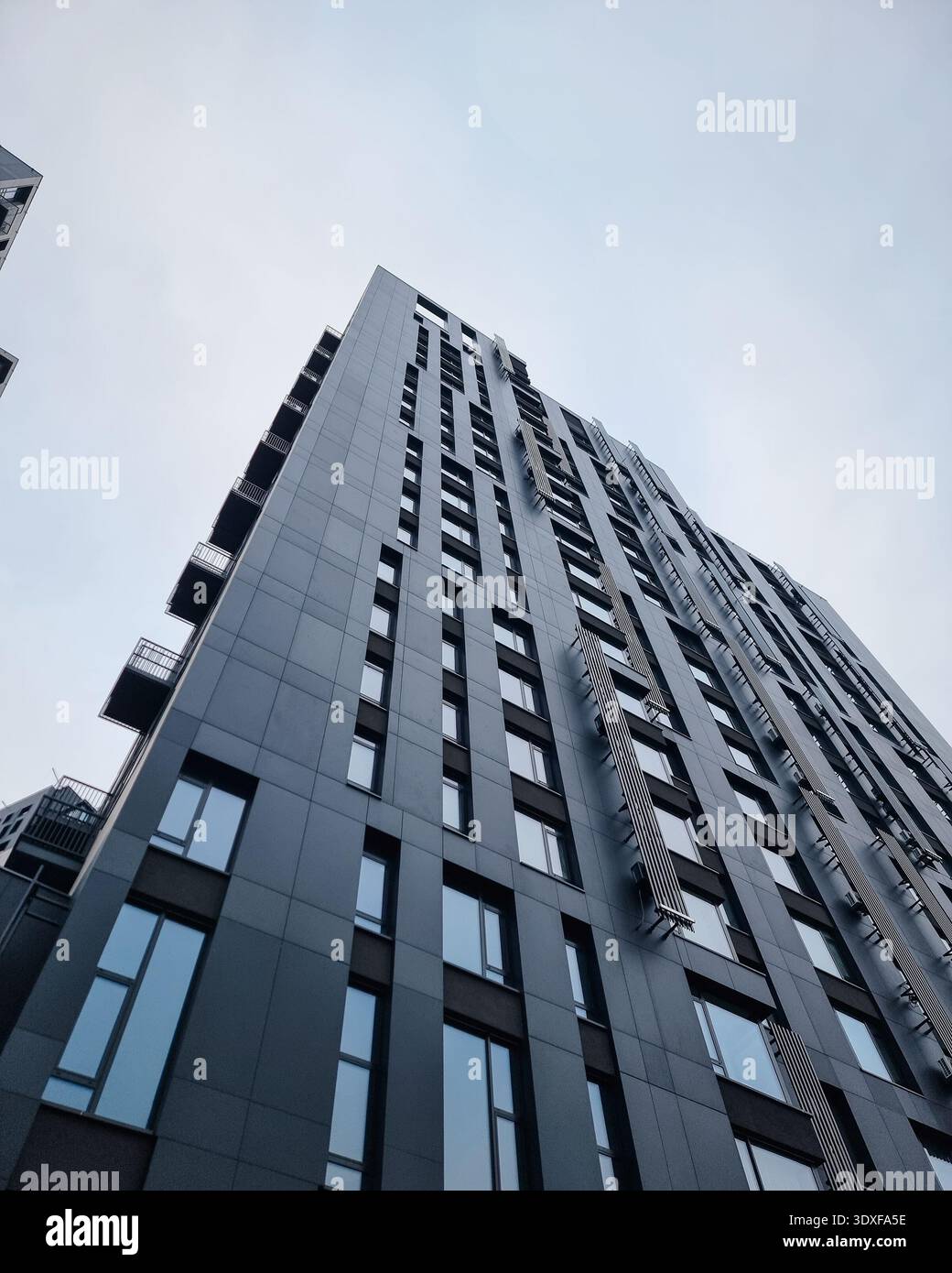 Moderno edificio grigio scuro con un cielo blu chiaro. Foto ad angolo basso di alti appartamenti contemporanei con facciata a carbone e finestre alte e strette. Foto Stock