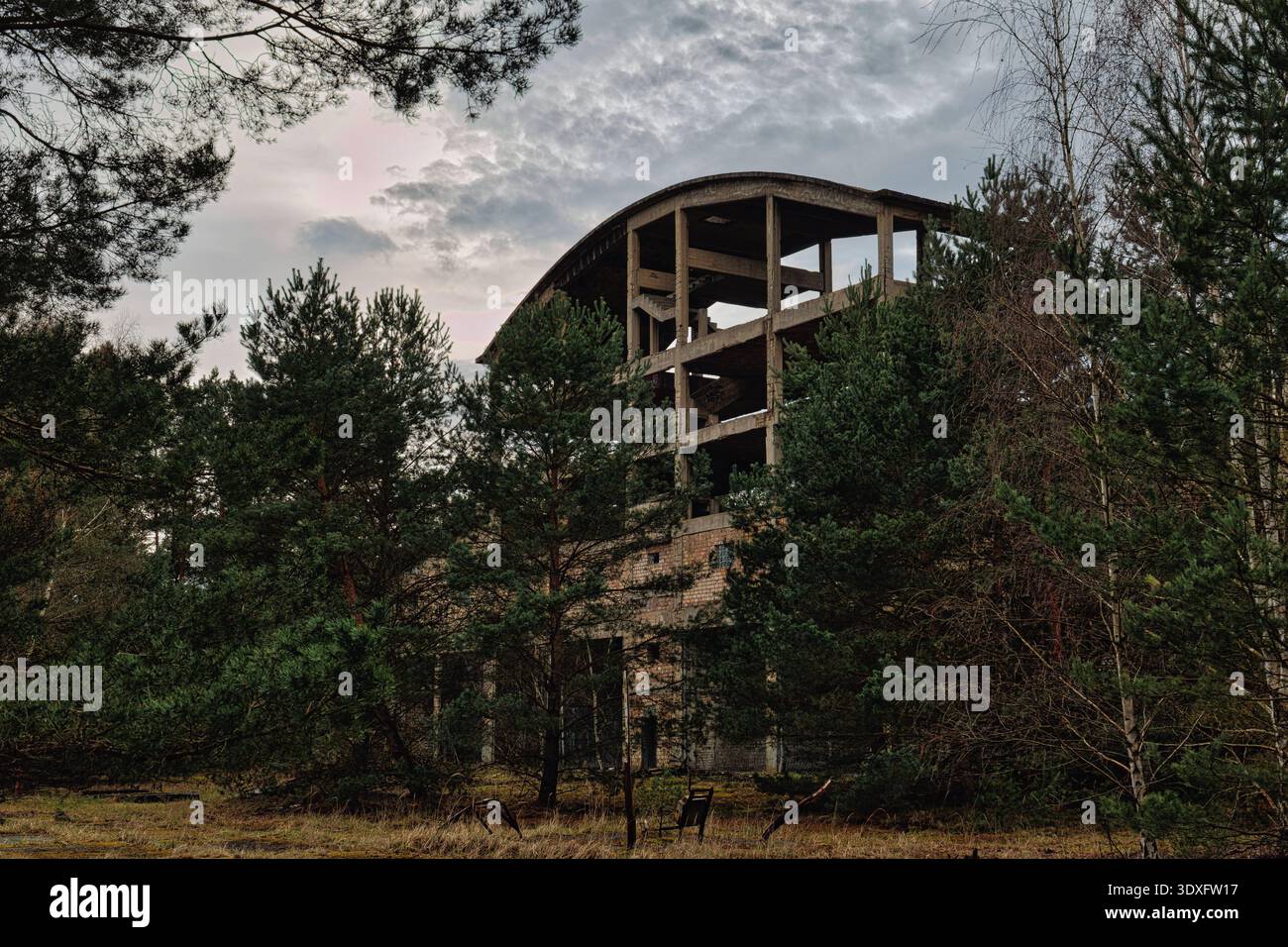 Immagine ampia di un sito industriale abbandonato o di un complesso militare in una foresta, con strutture in cemento in decadenza e muri in mattoni sotto un cielo nuvoloso. Foto Stock