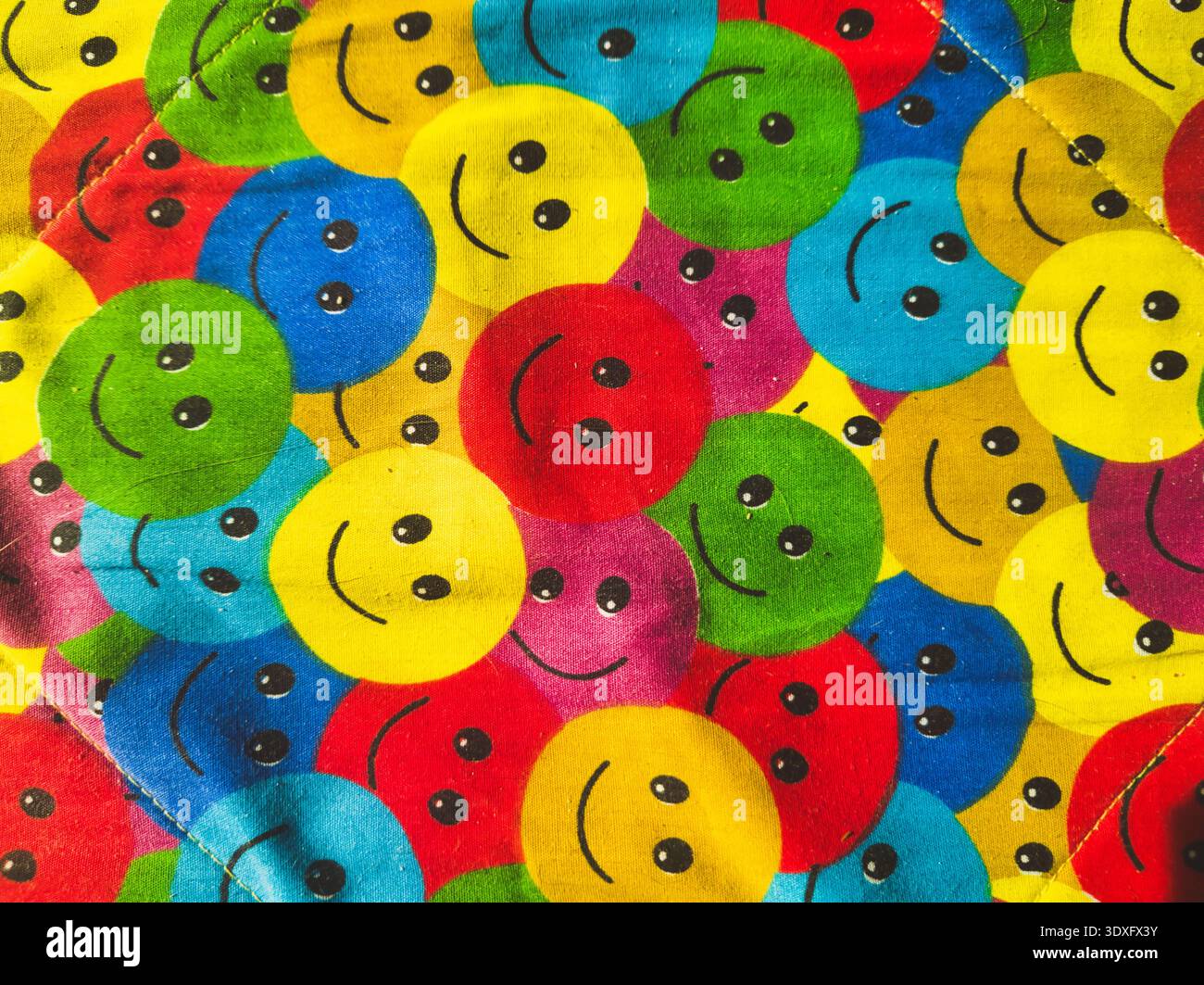 Un'immagine top-down di alta qualità di tessuto trapuntato con ripetute icone di colore giallo, rosso, blu e verde Happy Face. Questo modello allegro e nostalgico lo è Foto Stock