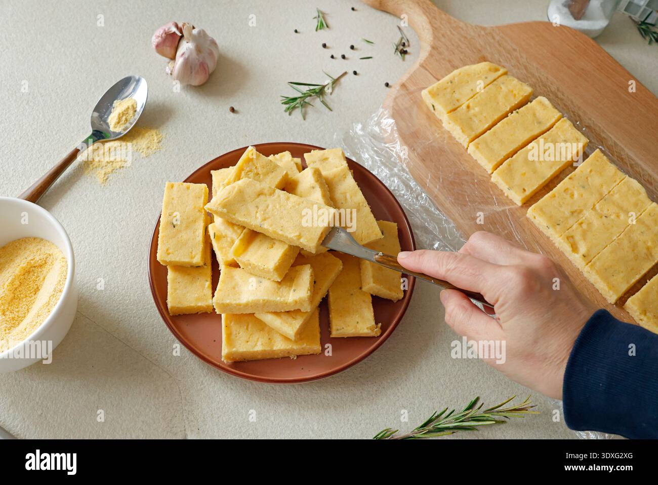 Una persona anonima posiziona delle fette di polenta dura sulla piastra. Farina di mais in cucina. Ingredienti e cucina tradizionale italiana. Foto Stock
